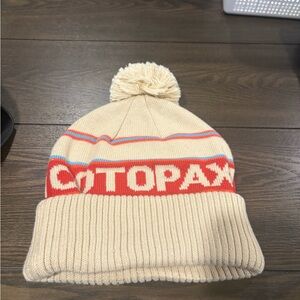 Cotopaxi Cumbre Beanie in cream with a fold-over cuff and pom-pom.